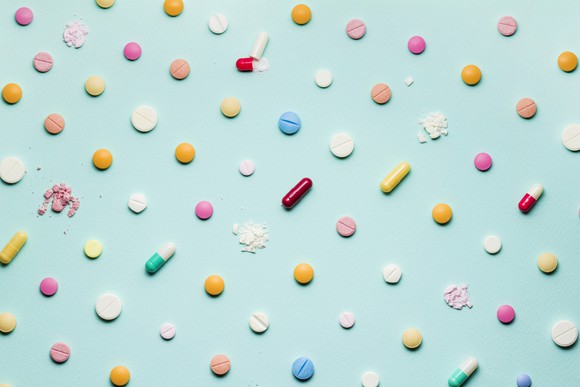 Many different pills and capsules on a blue background, with some of the pills crushed
