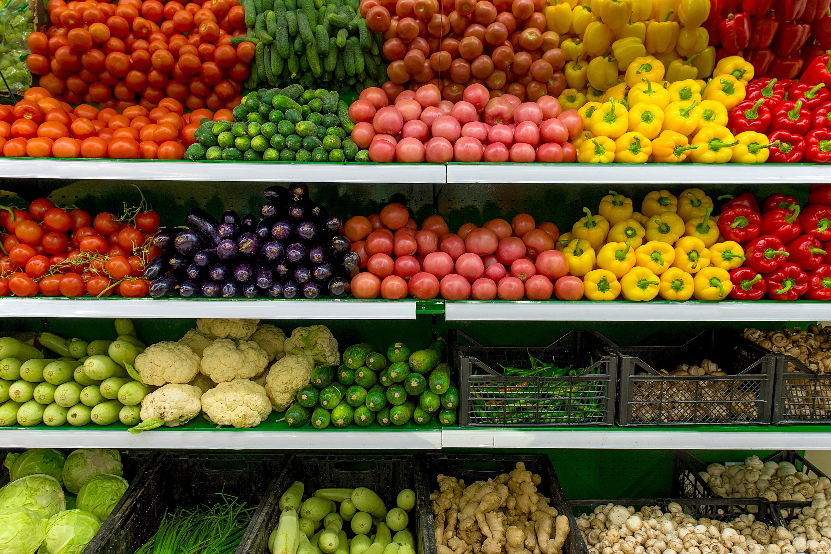 Shelves of vegetables in a supermarket, including peppers, tomatoes, eggplants, cauliflower, ginger, and more