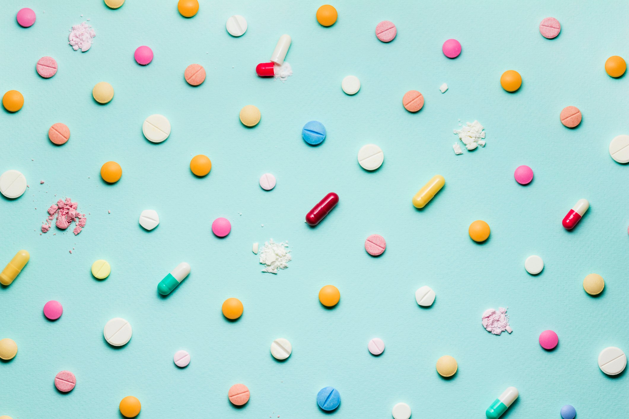Many different types of pills and capsules, some crushed, laid out in a neat pattern