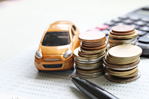 Miniature car next to stack of coins and calculator