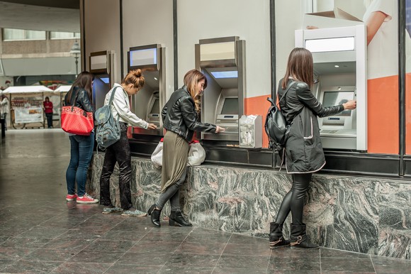 Several women use a row of ATMs.
