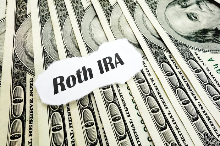 The words "Roth IRA" written on a piece of paper sitting atop a pile of cash.