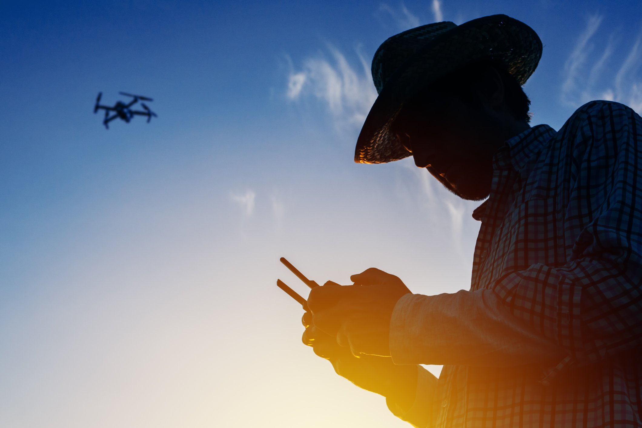 Silhouette of a farmer flying a drone with a remote control
