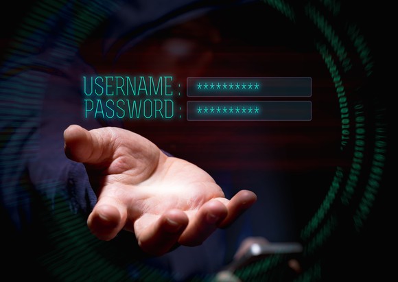 A hooded hacker reaches toward the words "username" and "password" on a screen.