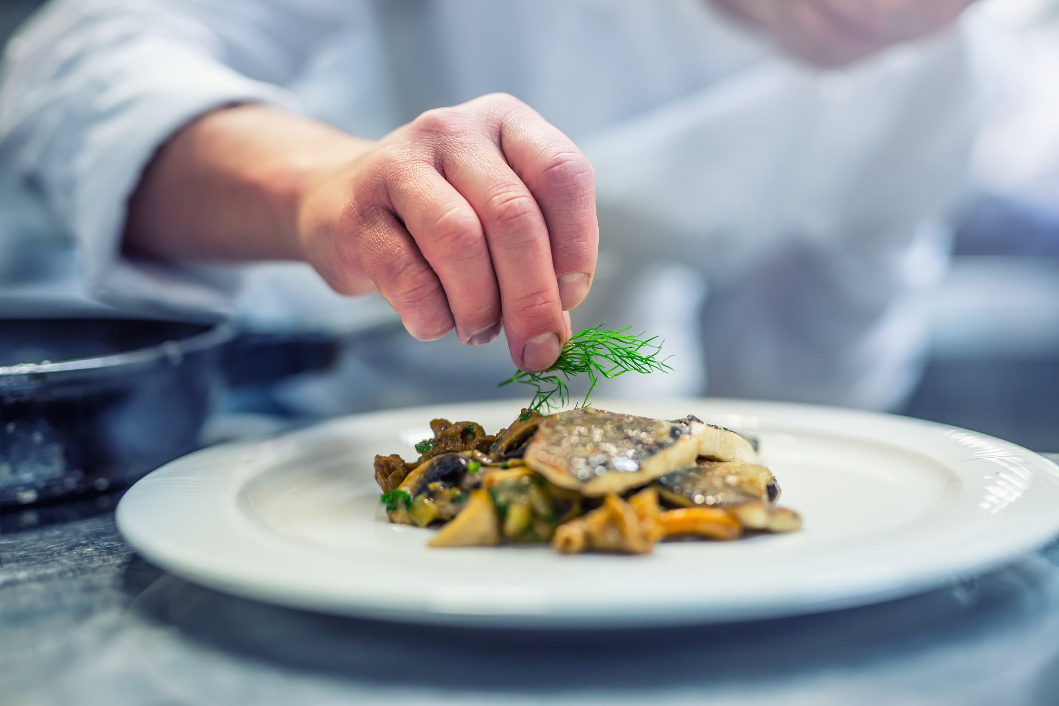 A chef garnishes a plated meal.