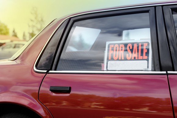 A red car with a "for sale" sign in a rear side window.
