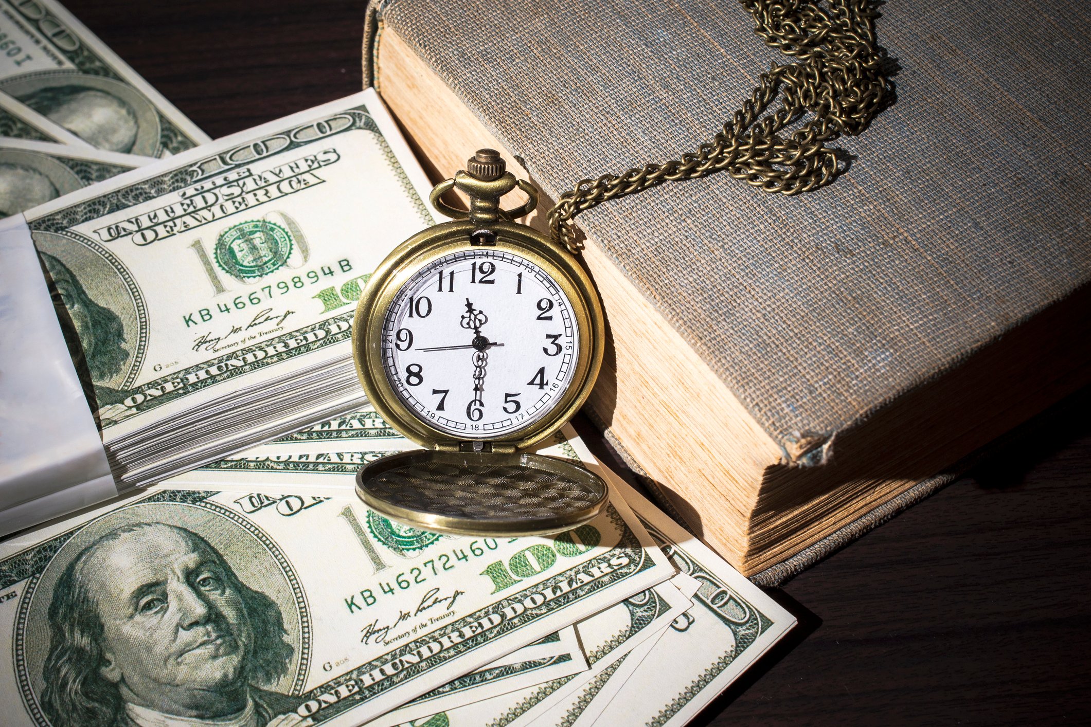 Pocket watch and book next to $100 bills