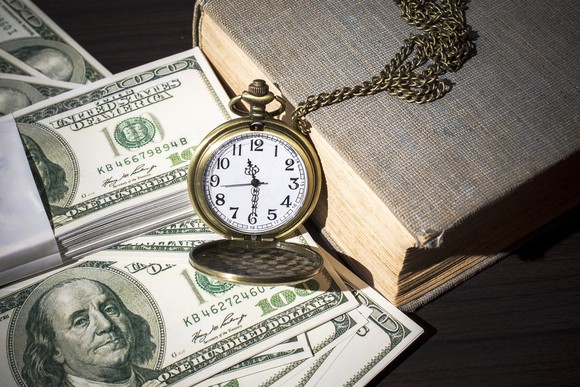 Pocket watch and book next to $100 bills