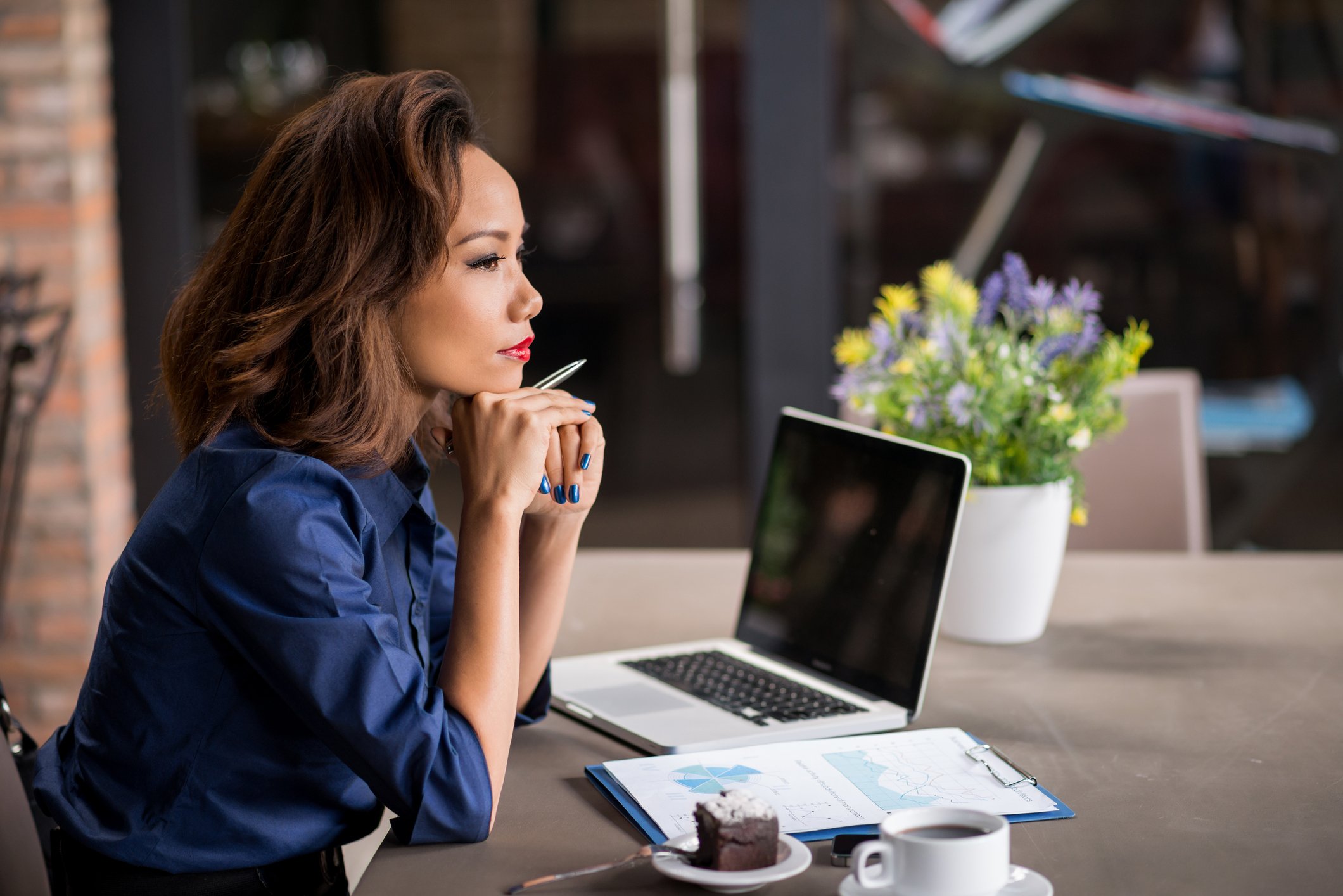 A woman thinking in front of a laptop and some documents