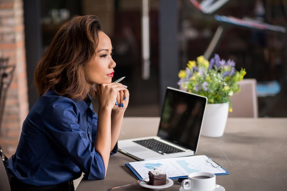 A woman thinking in front of a laptop and some documents