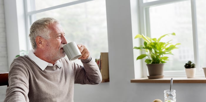 An older man sitting at a table drinking coffee.