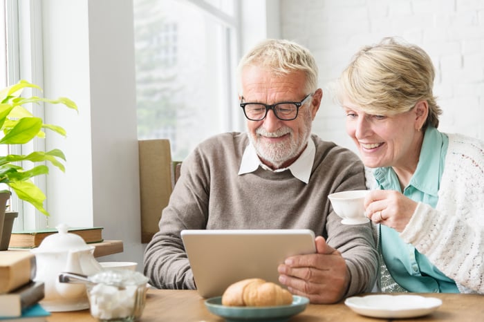 An older couple sitting at a table using a tablet and drinking coffee.