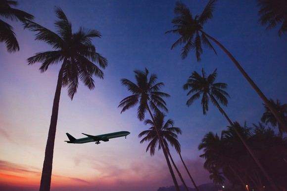 A plane flying at sunset over palm trees