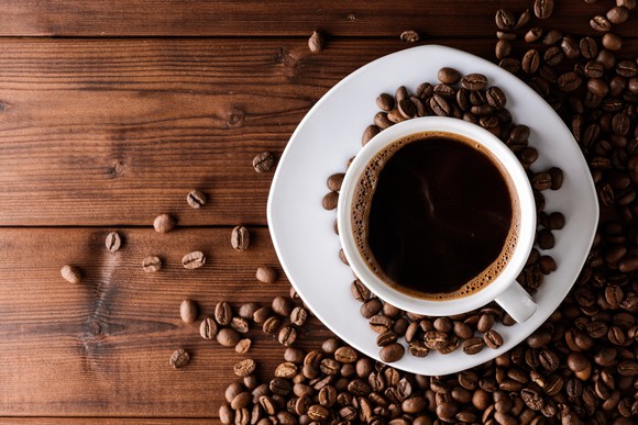 Cup of coffee on saucer on a wooden table with coffee beans scattered around it