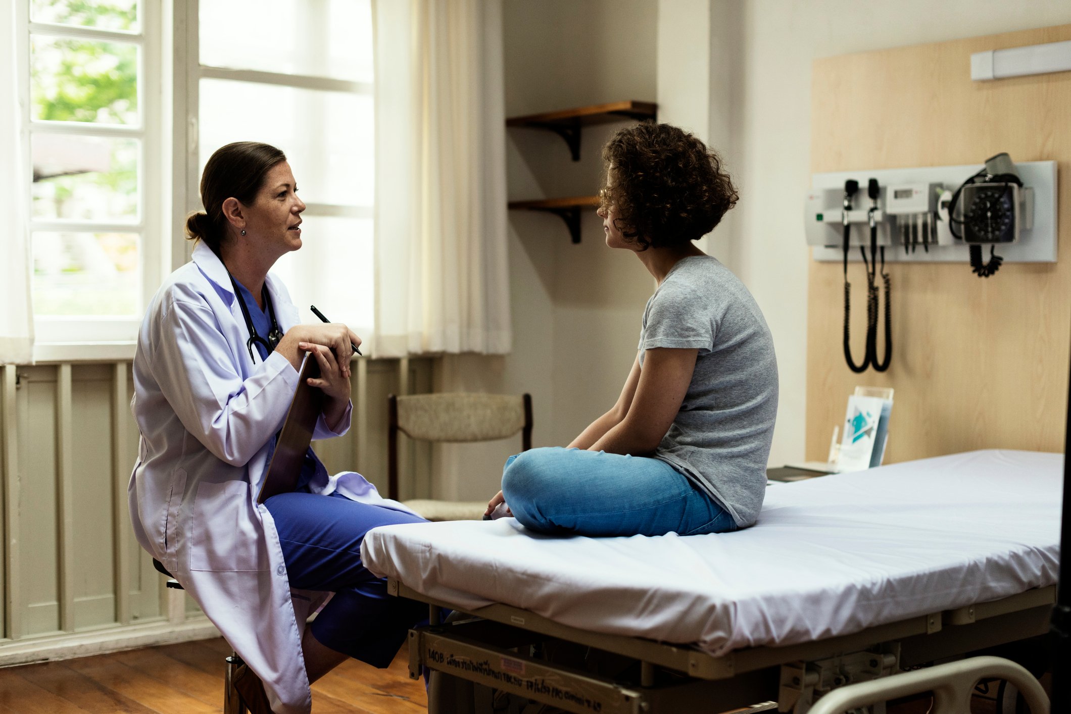 Doctor in a chair talking to a patient on an examination table.
