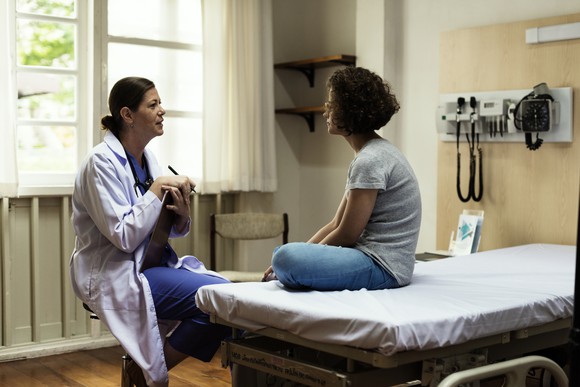 Doctor in a chair talking to a patient on an examination table.