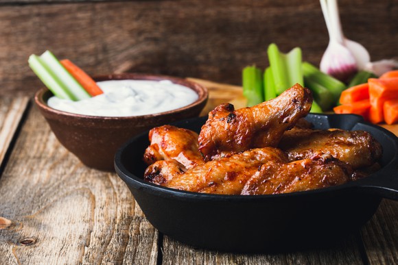 Chicken wings with carrots, celery sticks, and dipping sauce on rustic wooden table