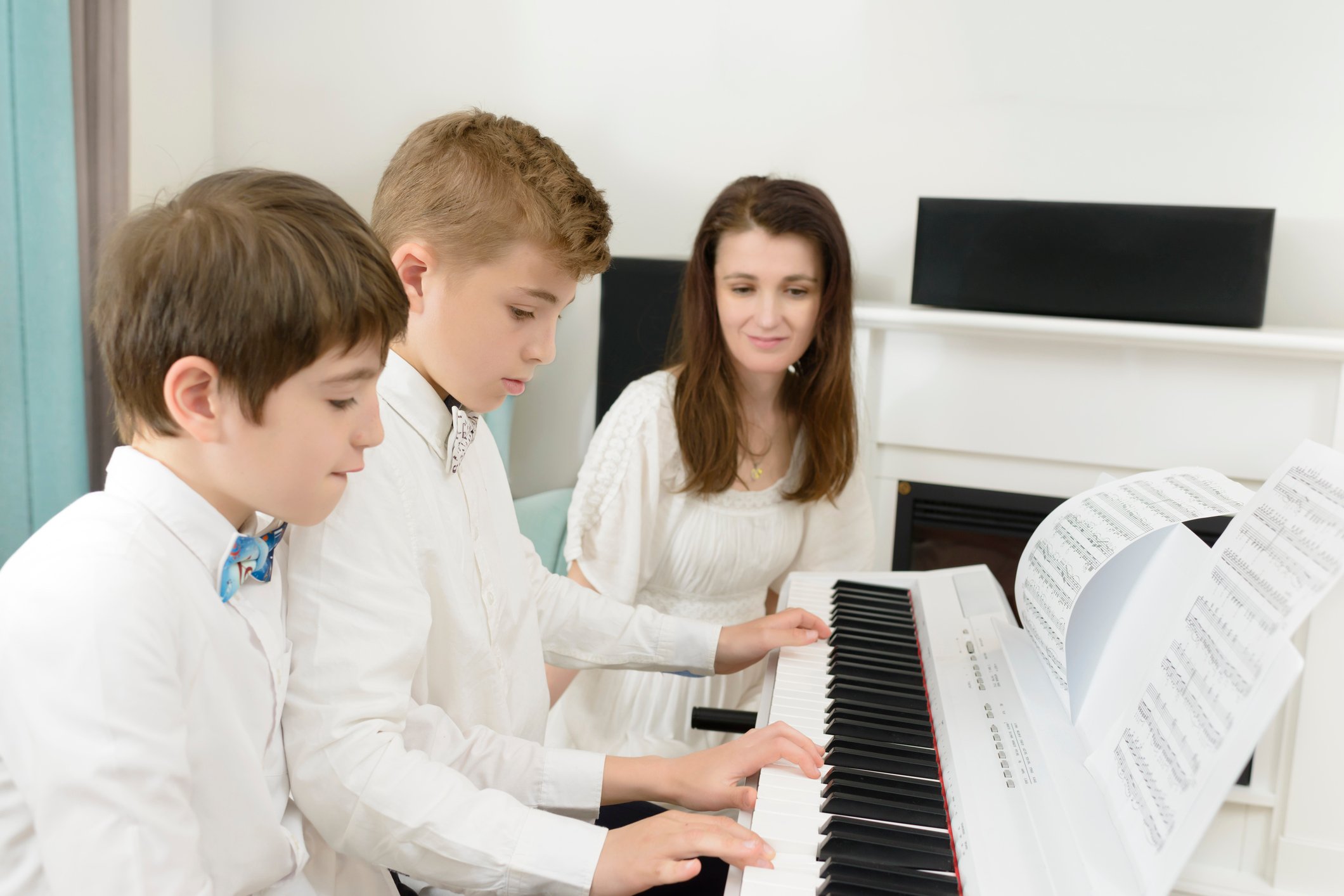 Music teacher teaching two boys how to play the piano.