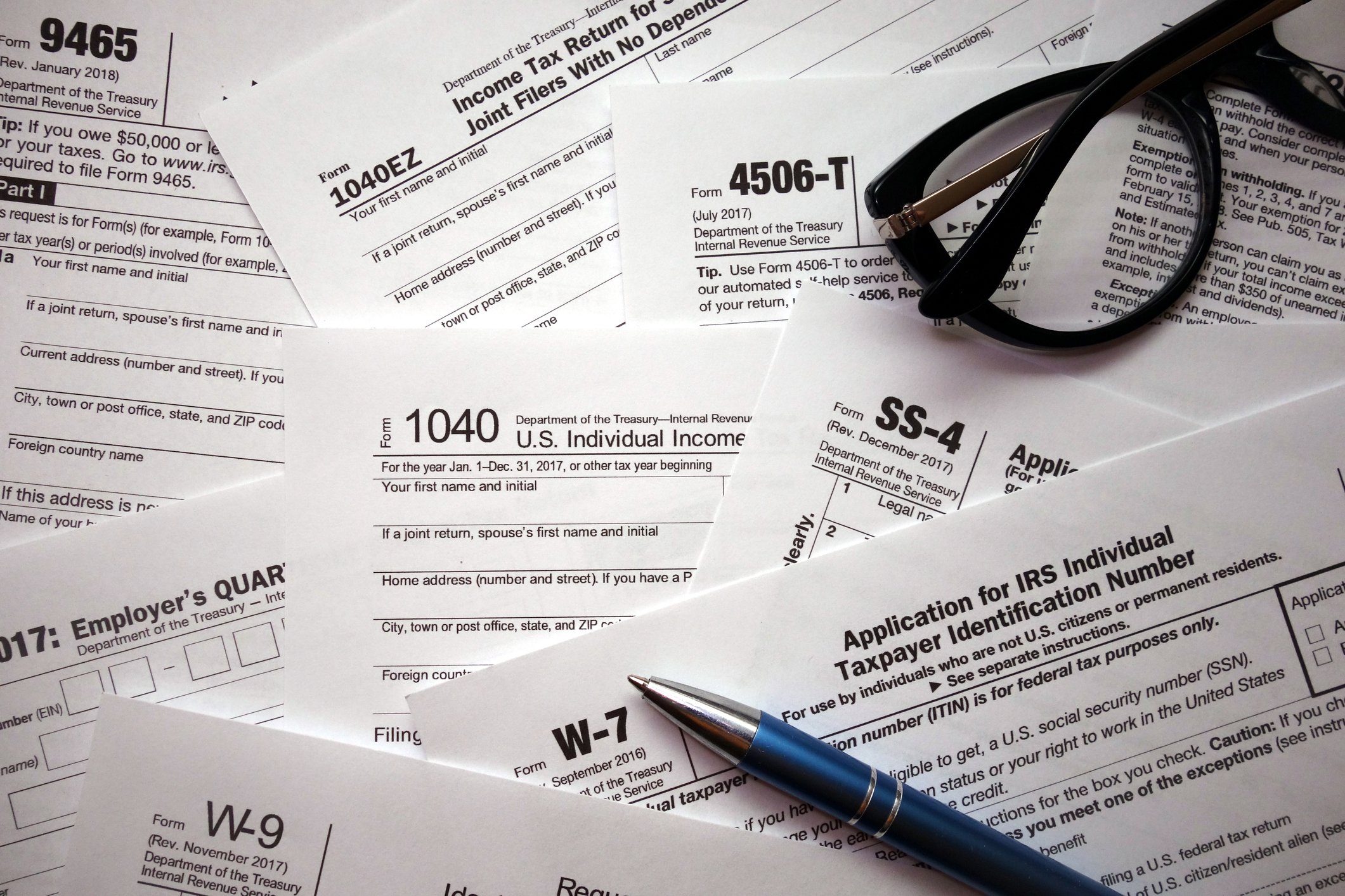 An assortment of tax forms with a pen and a pair of glasses