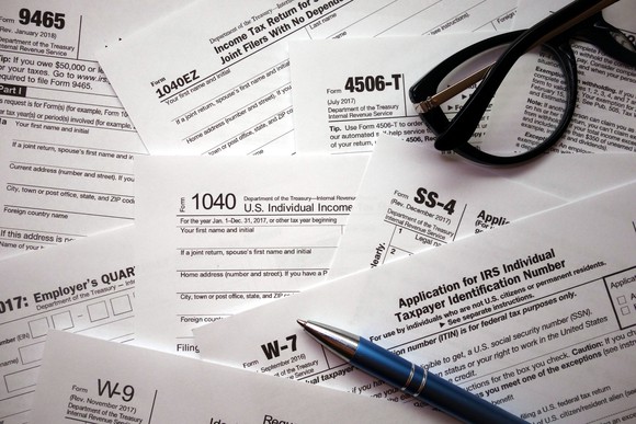 An assortment of tax forms with a pen and a pair of glasses