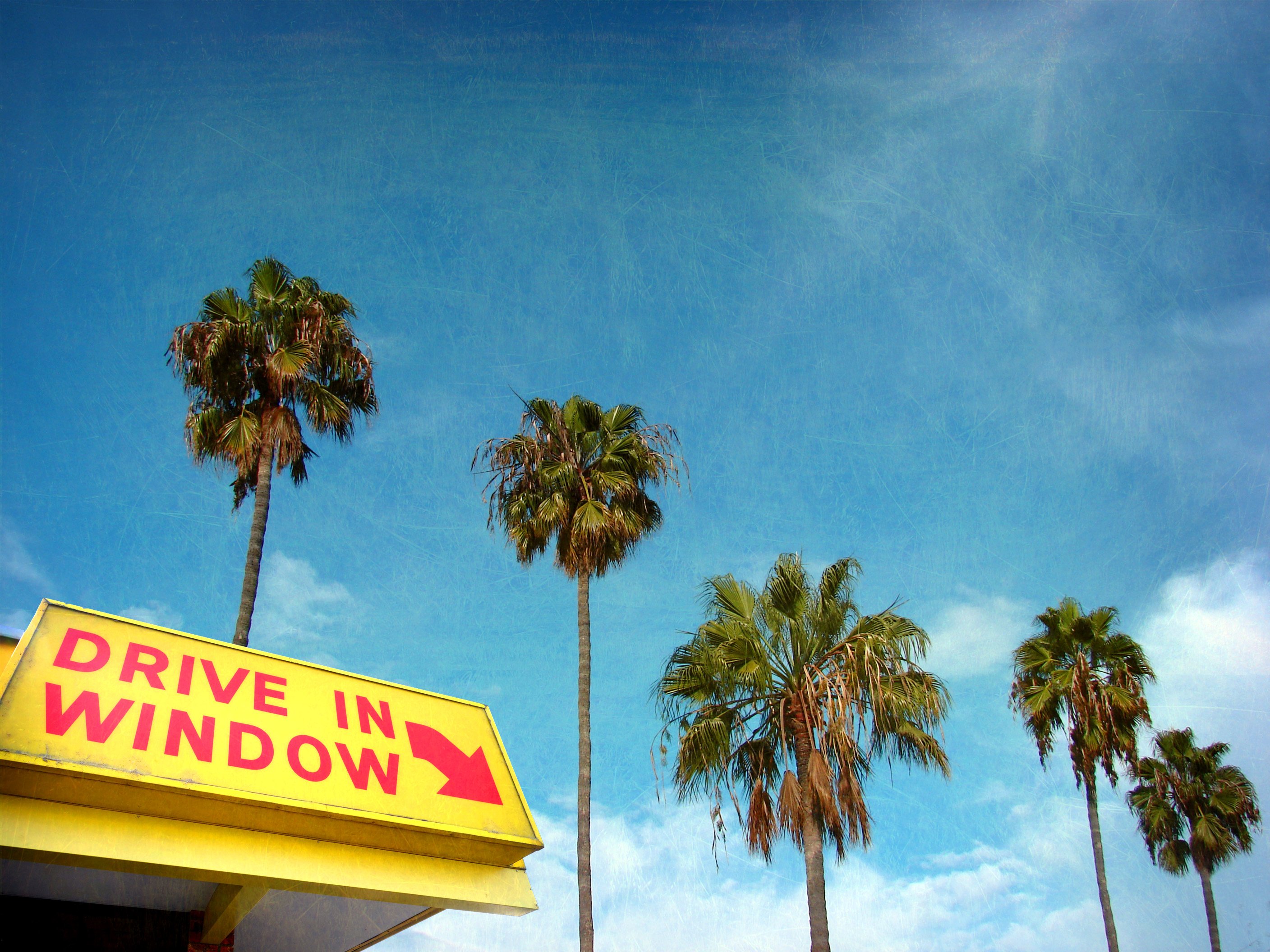 A sign pointing to the drive-in window with palm trees behind it