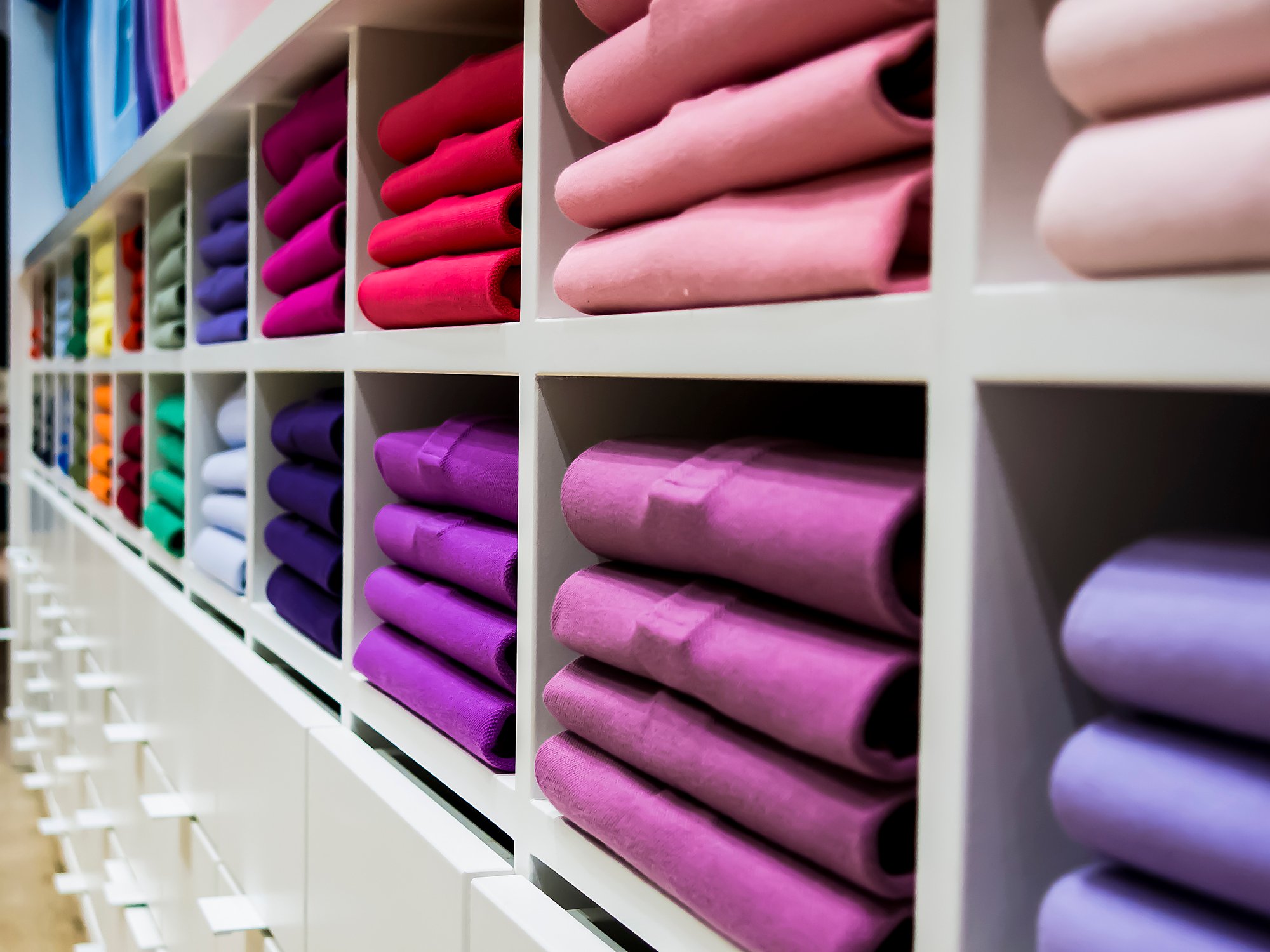 Folded piles of colorful t-shirts in display cubbies at a store