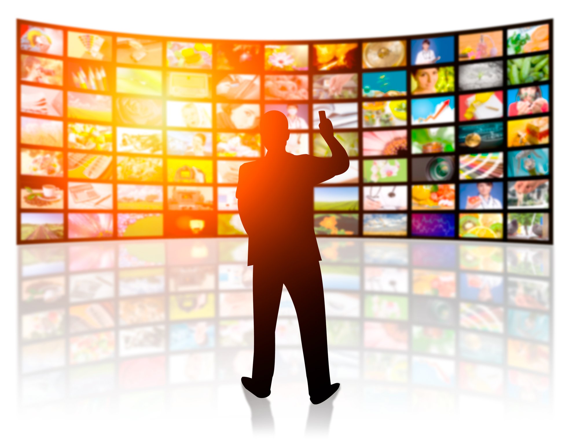 Silhouette of a man holding a remote and standing in front of many screens