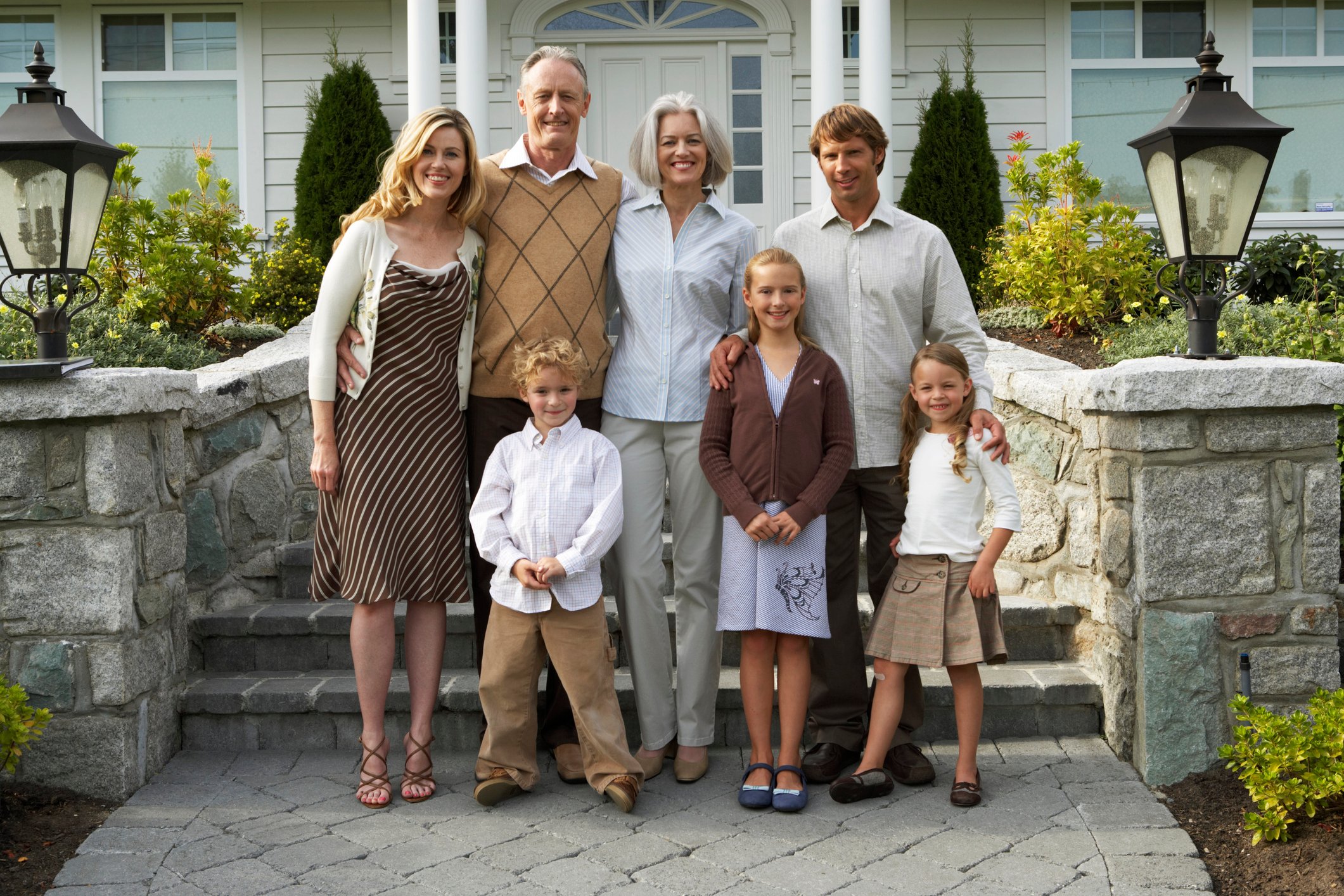 Three generations of a white, middle-class family stand in front of their home