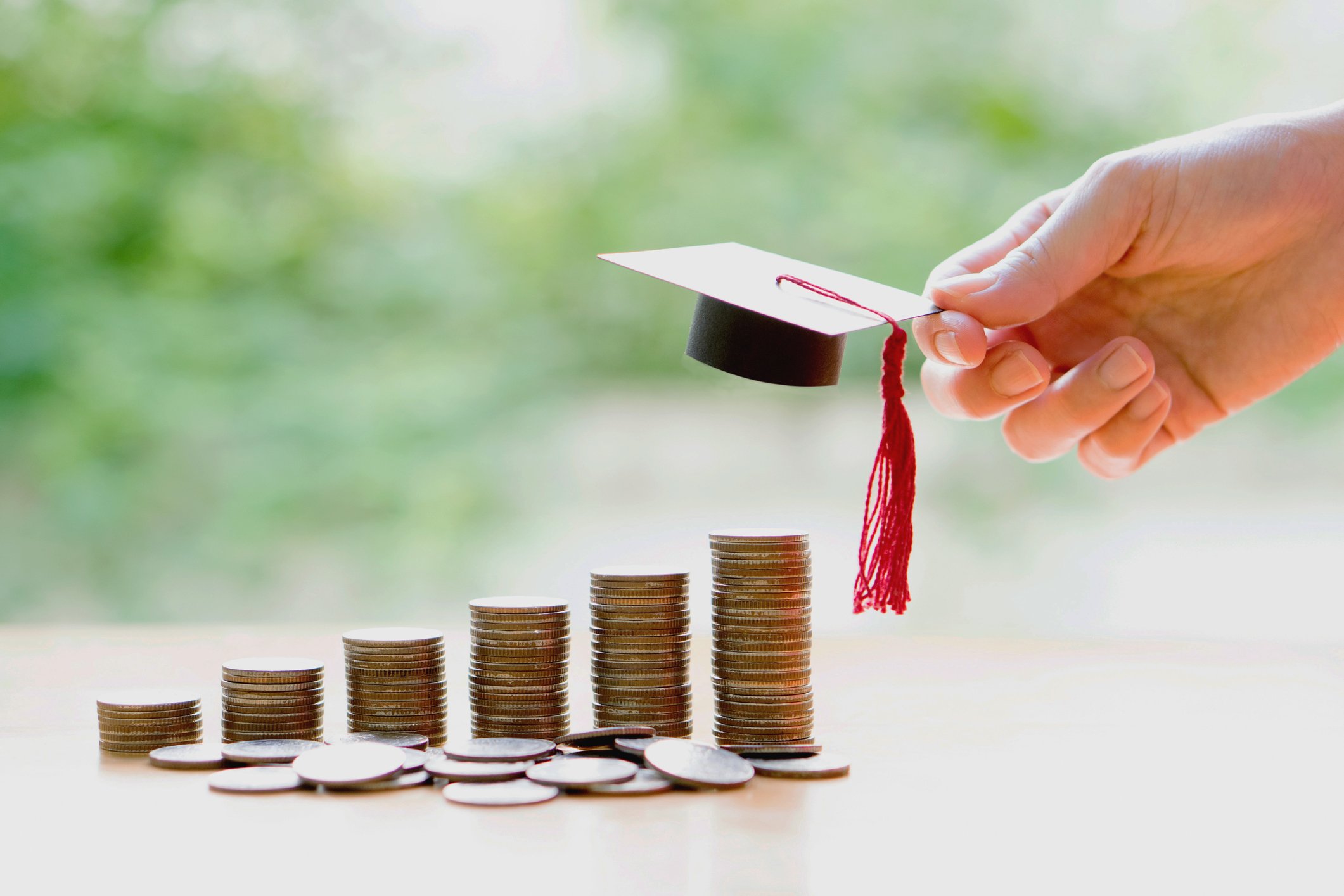 Stacks of coins with a hand placing a miniature mortarboard on the tallest one