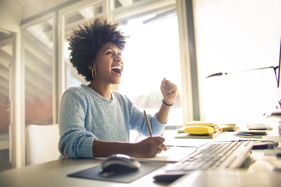 A woman celebrates the great news she sees on her computer