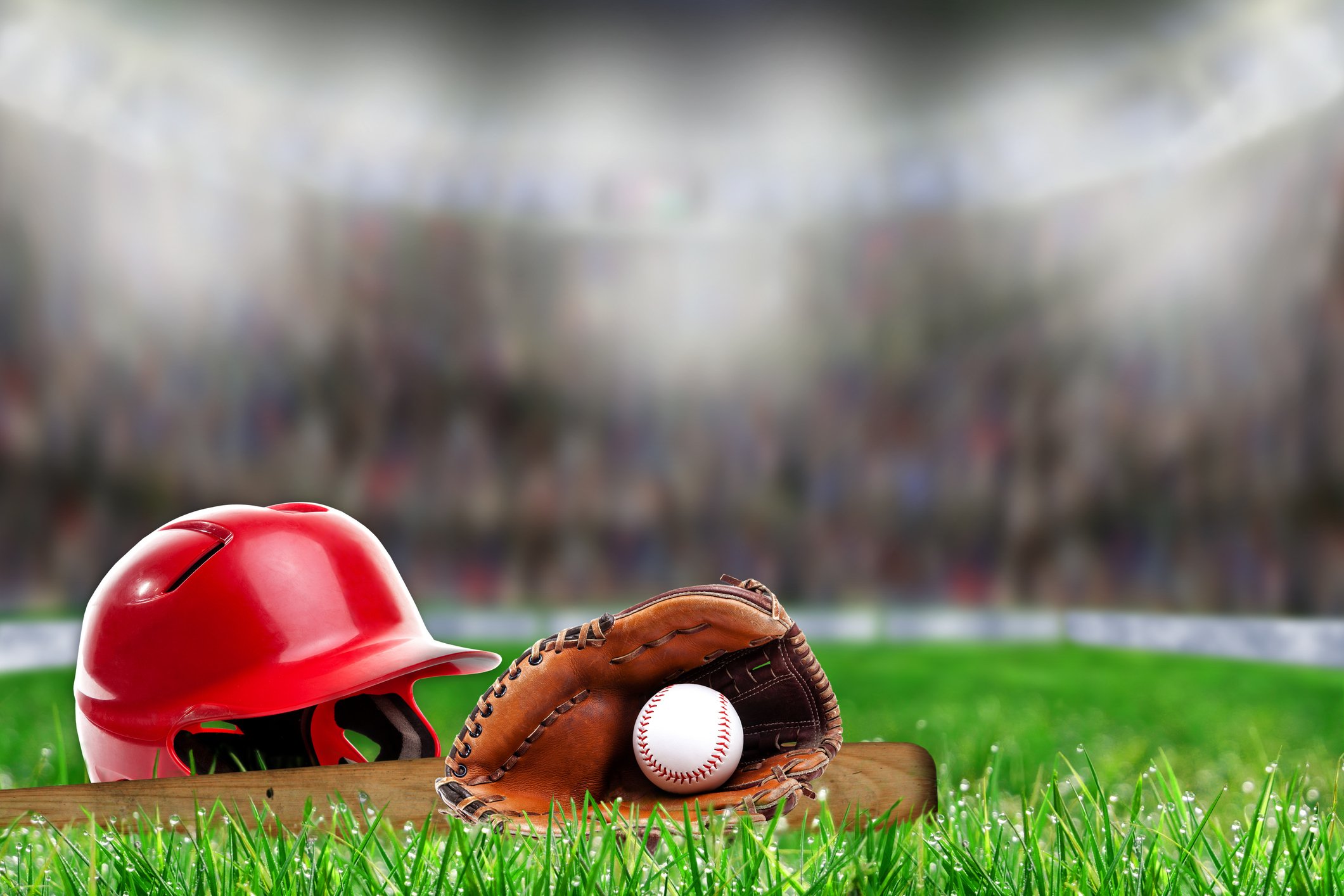 A baseball helmet, glove, ball, and bat on the field in a stadium.