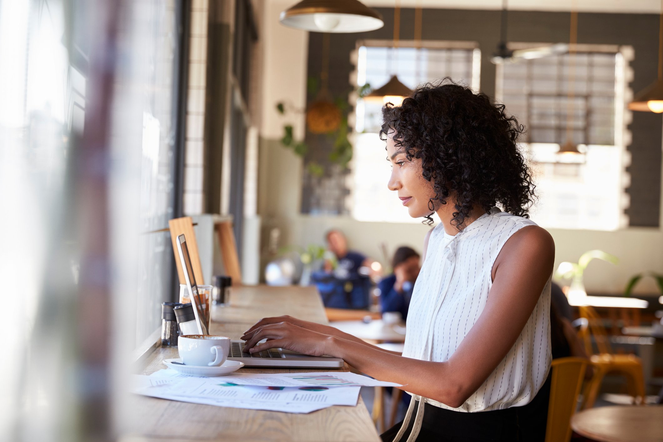 A businesswoman works at a laptop by the window in a coffeeshop.