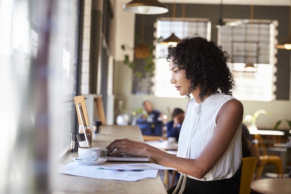 A businesswoman works at a laptop by the window in a coffeeshop.