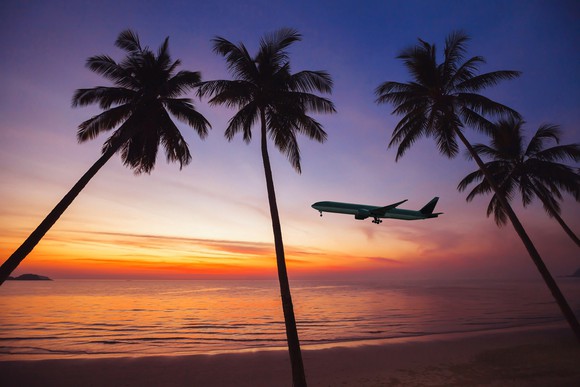 An airplane silhouetted against a tropical sky at sunset, with palms in the foreground