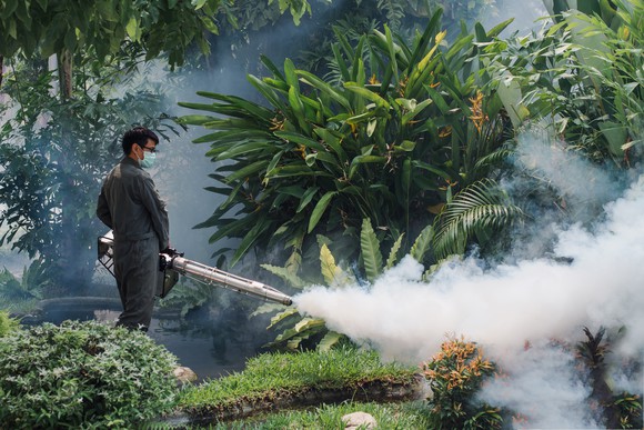 A man in a mask uses a fogger machine to spray for mosquitos.