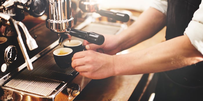 A barista in an apron using an espresso machine behind the counter