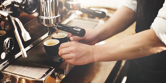 A barista in an apron using an espresso machine behind the counter