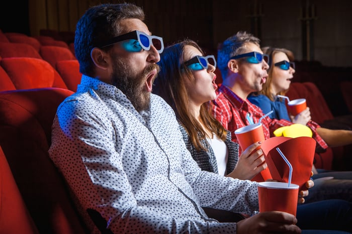 Four people in a movie theatre wearing 3D goggles with surprised looks on their faces.