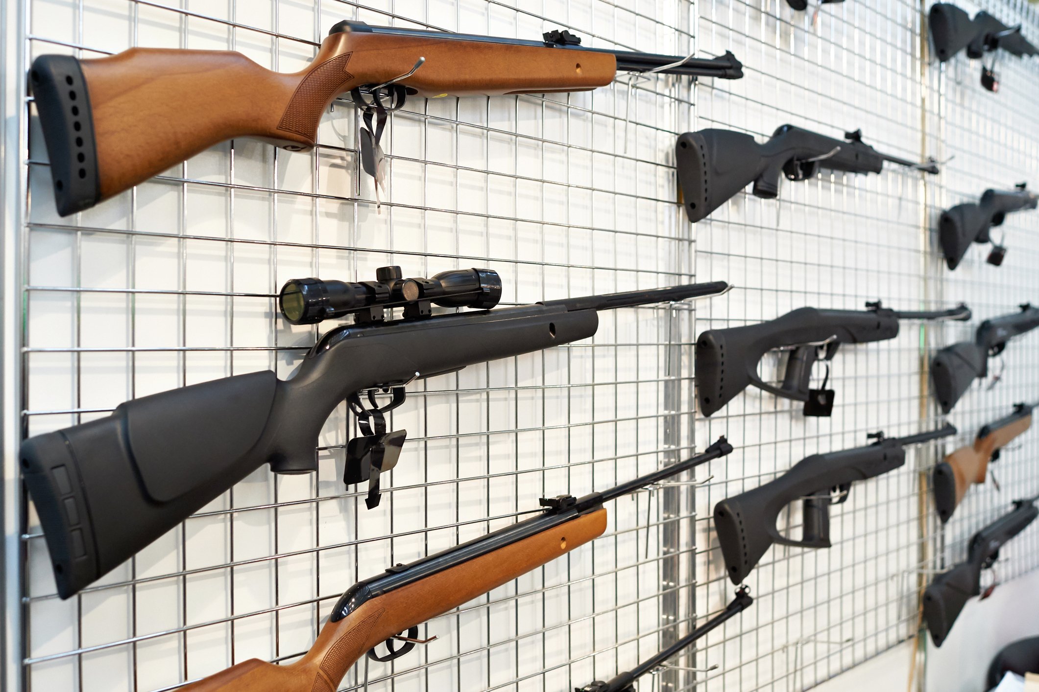 A white wall with various different rifles hanging on it.