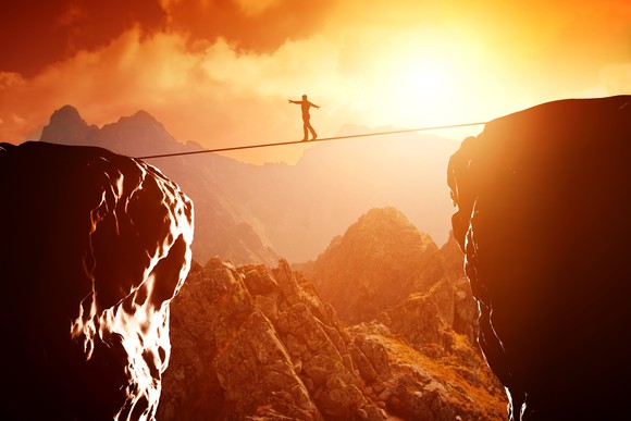 Man walking on tightrope between two cliffs with sun setting in the background