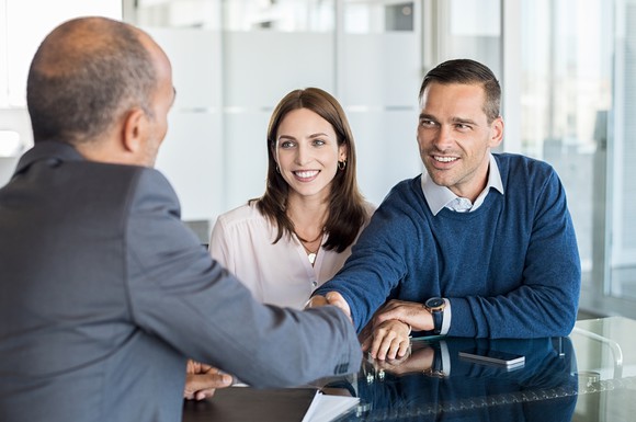 A financial advisor shakes hands with a client couple.