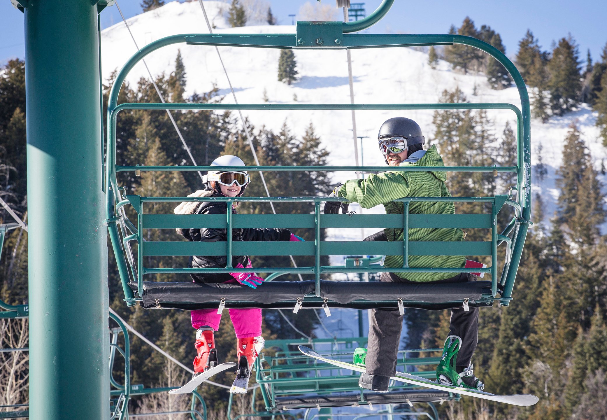 Adult and child on a ski lift with trees and hill in background