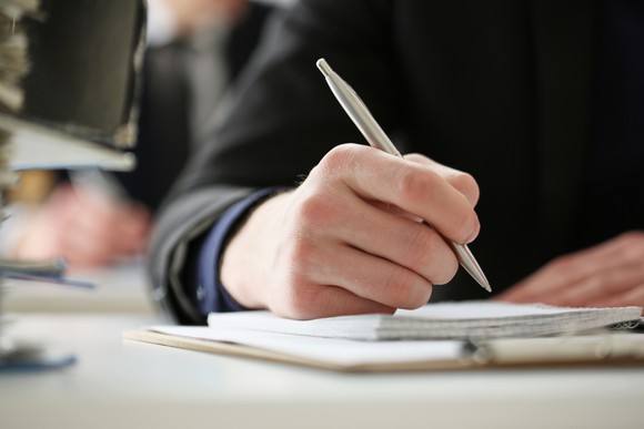 A close-up of a man's hand writing in a notebook