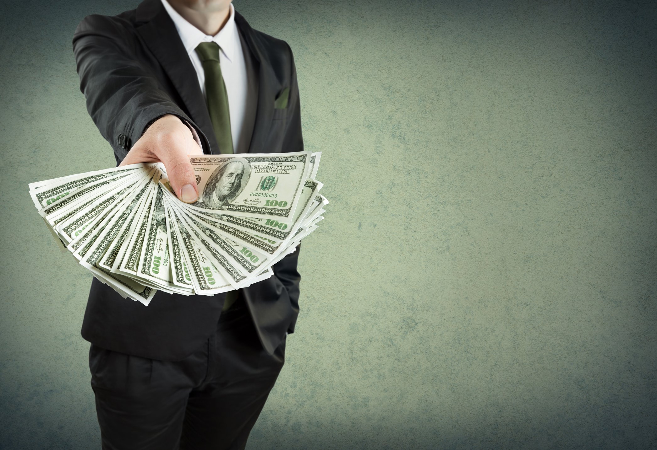Man in suit holding out fanned-out $100 bills