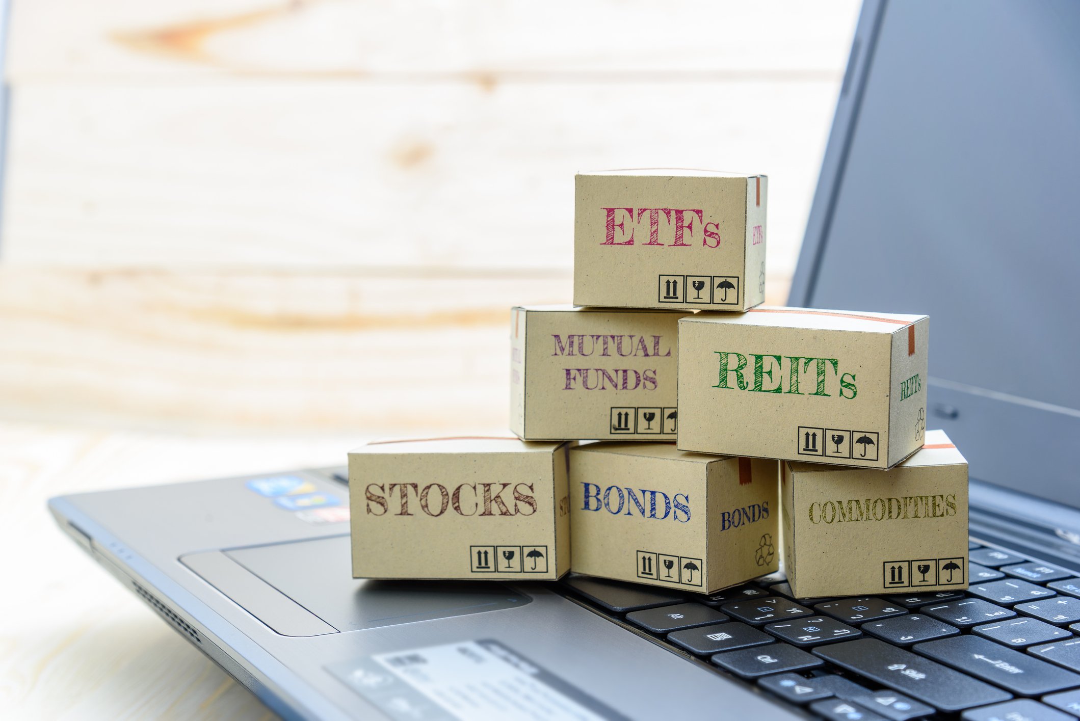 Small boxes labeled "STOCKS," "MUTUAL FUNDS," ETFs," etc., sitting on a laptop keyboard