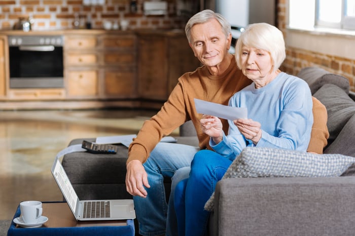 A retired couple sitting on a couch examine paperwork.