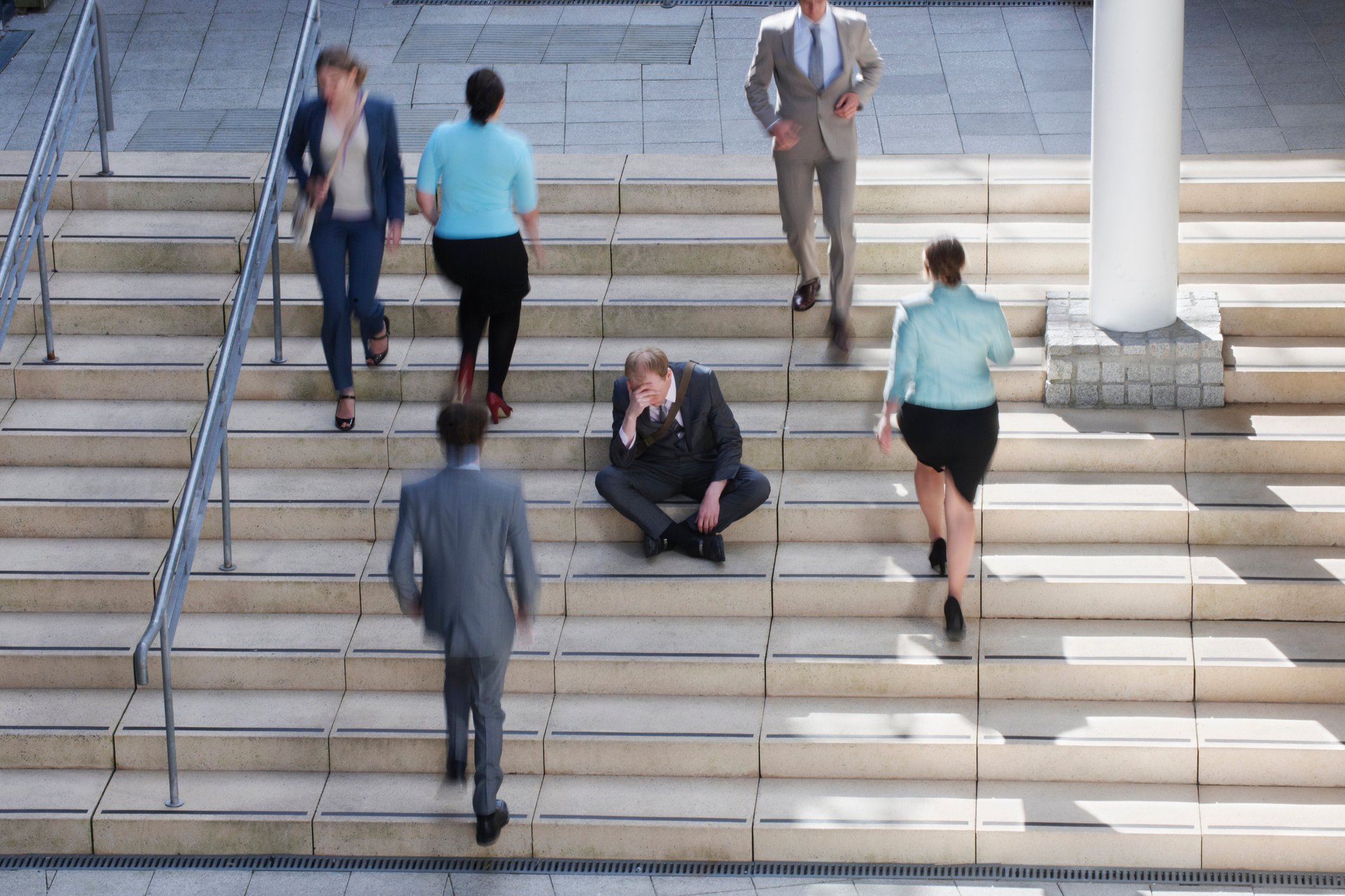 A man sitting on a staircase with people walking past him