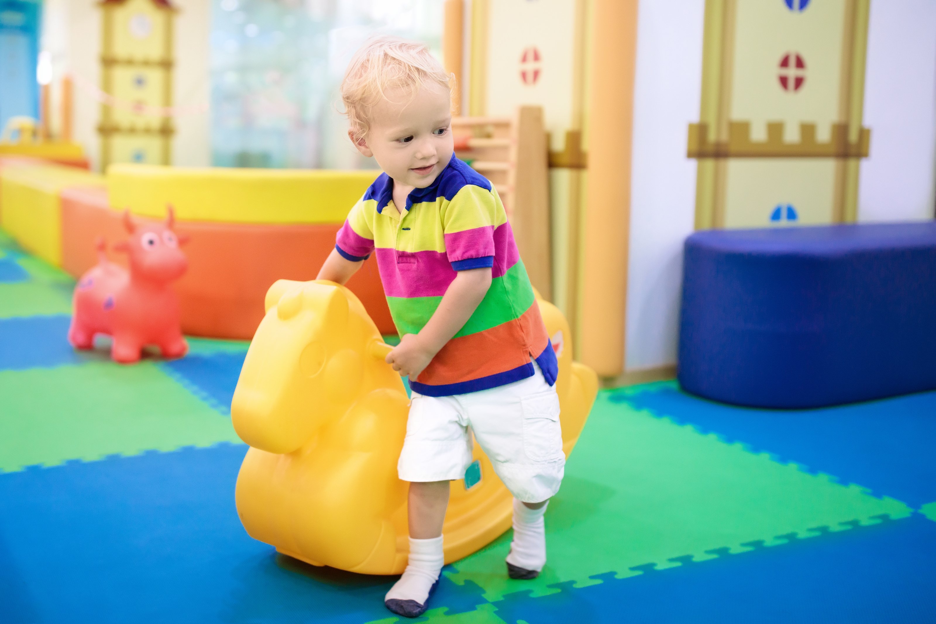 Little boy next to a rocking horse in a daycare setting