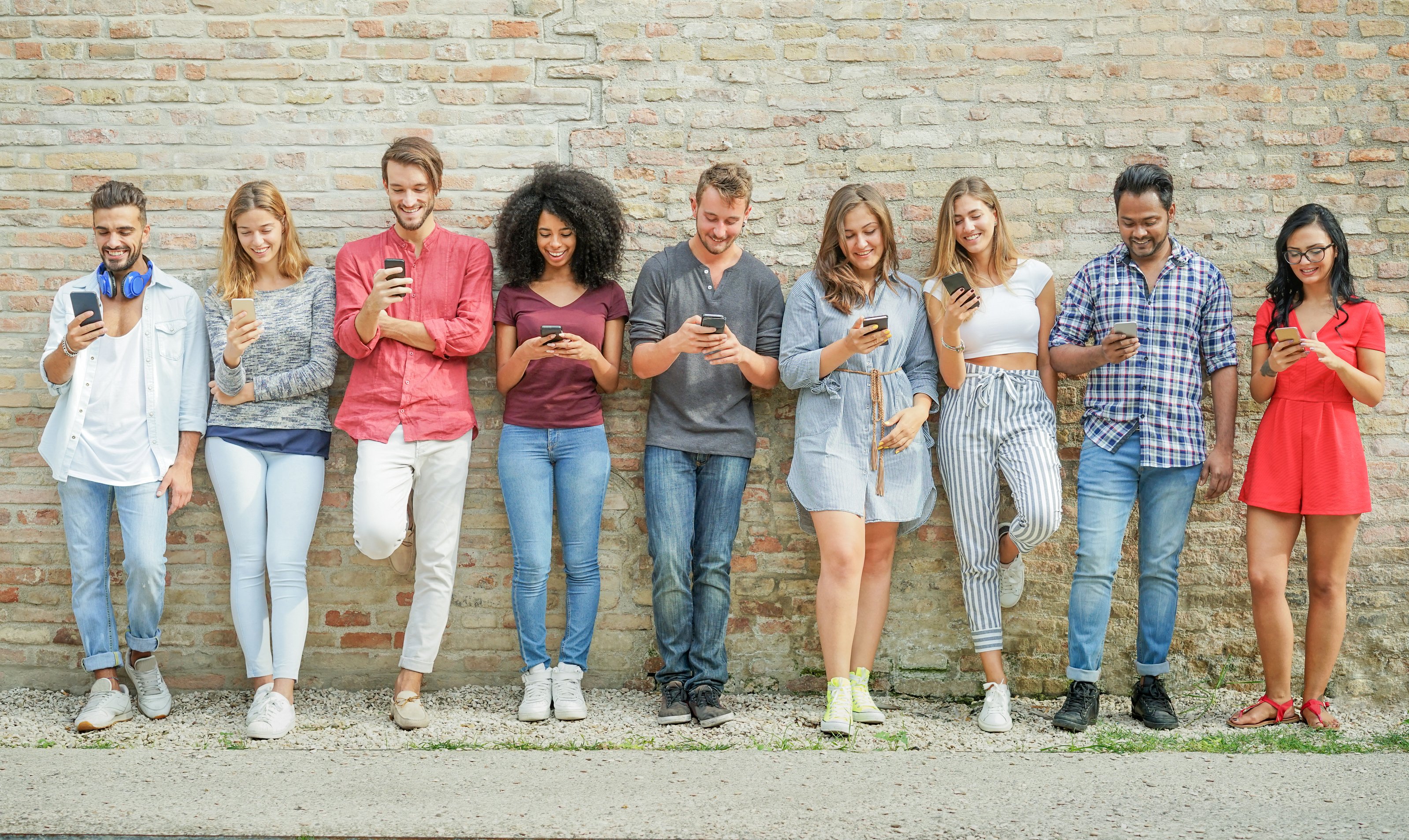 Nine young people leaning against a wall and looking at their smartphones