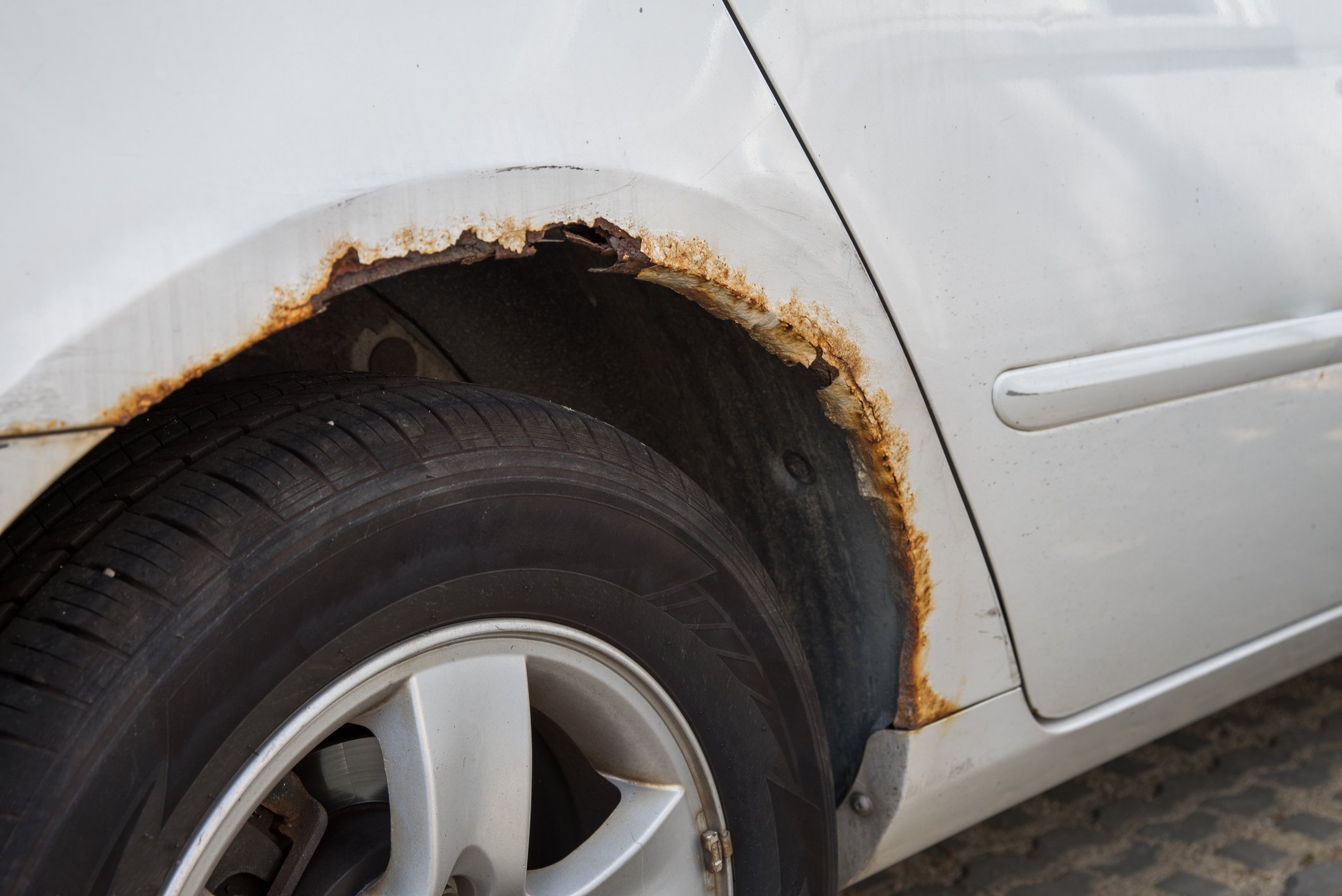A white car's rusty wheel well.